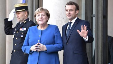 Emmanuel Macron and Angela Merkel wave to cameras on the threshold of a grand building
