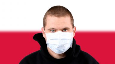 A man wearing a face mask stands in front of the Polish flag