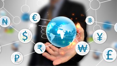A business person holds the globe, surrounded by currency symbols